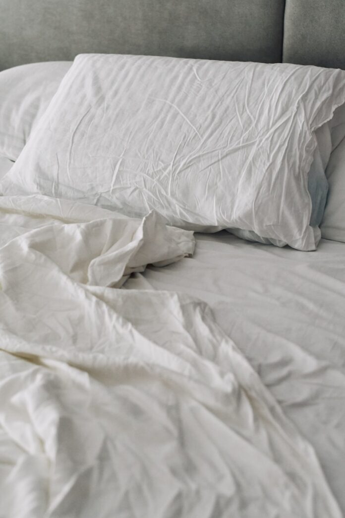 A rumpled white duvet and pillows on a bed.